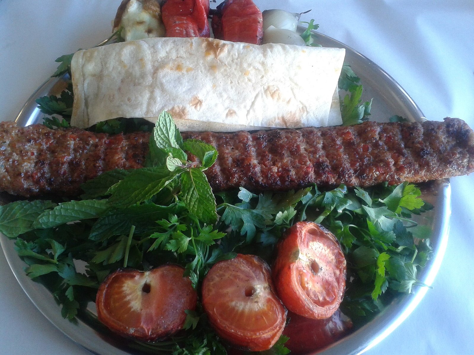 A plate of Adana kebab with flatbread, herbs and grilled vegetables