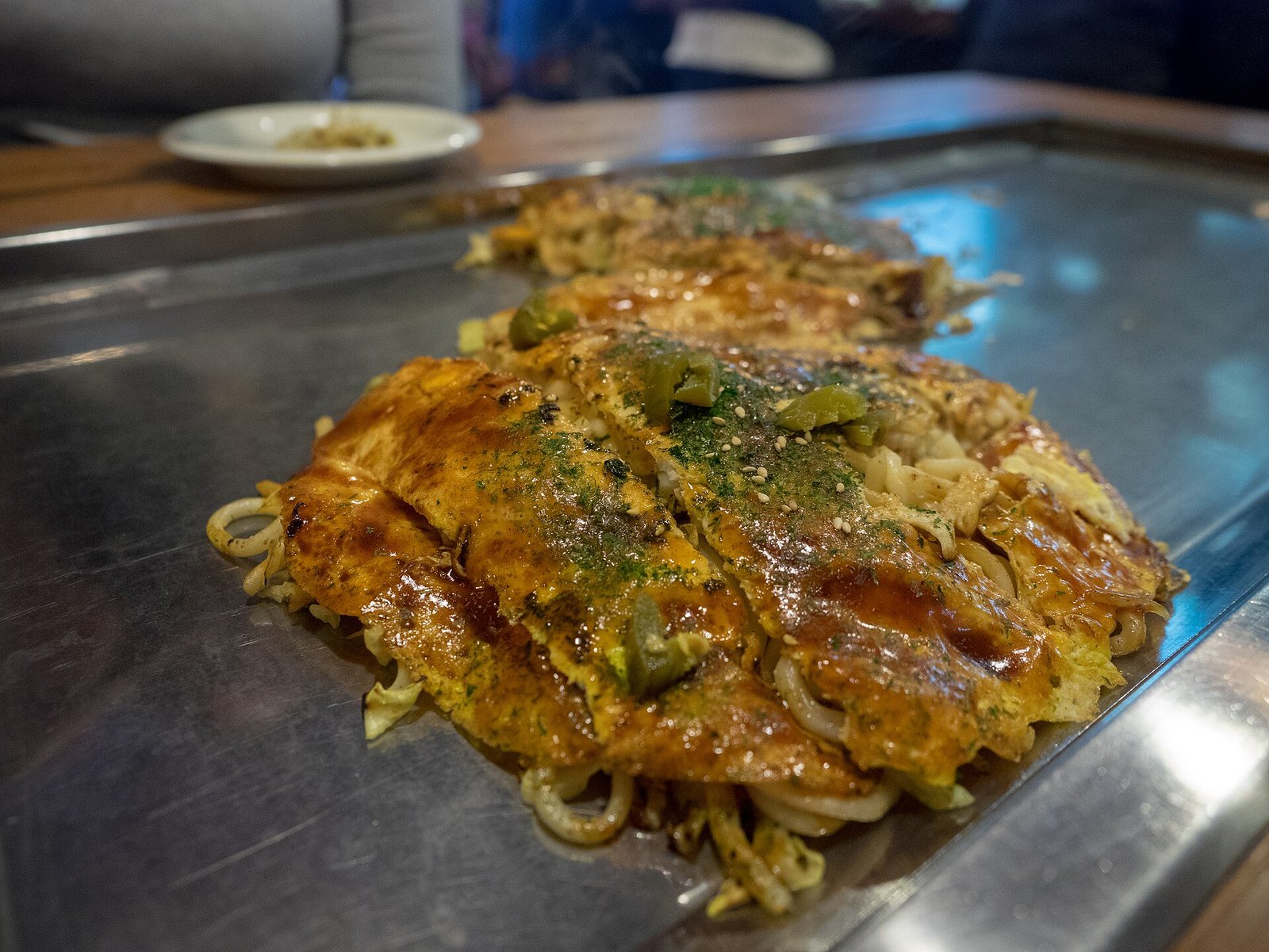 Hiroshima-style okonomiyaki cooking on a hotplate with noodles and sauce